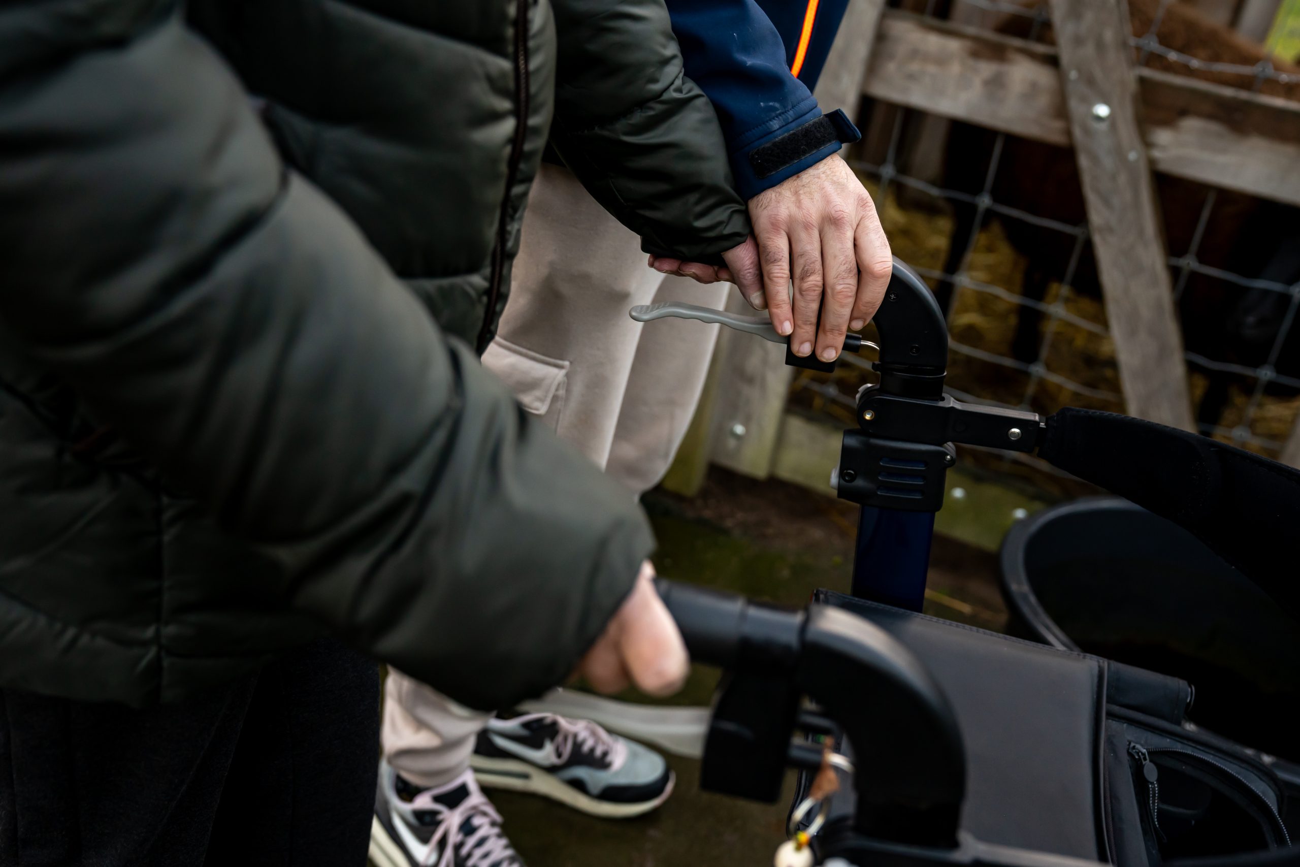 Close-up van handen op de handvatten van een rollator tijdens een wandeling buiten.