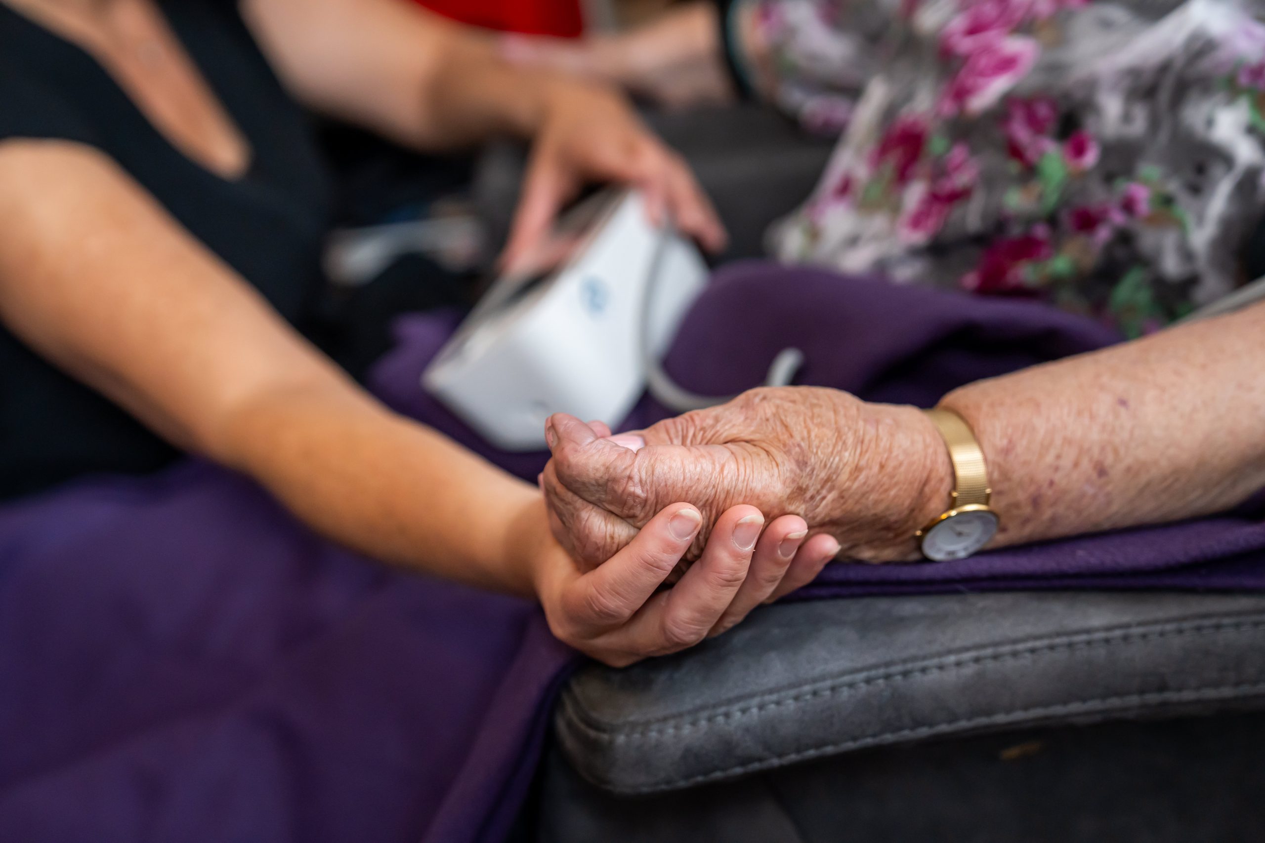 Jonge verzorger houdt liefdevol de hand van een oudere vrouw vast, symbool van zorg en steun.
