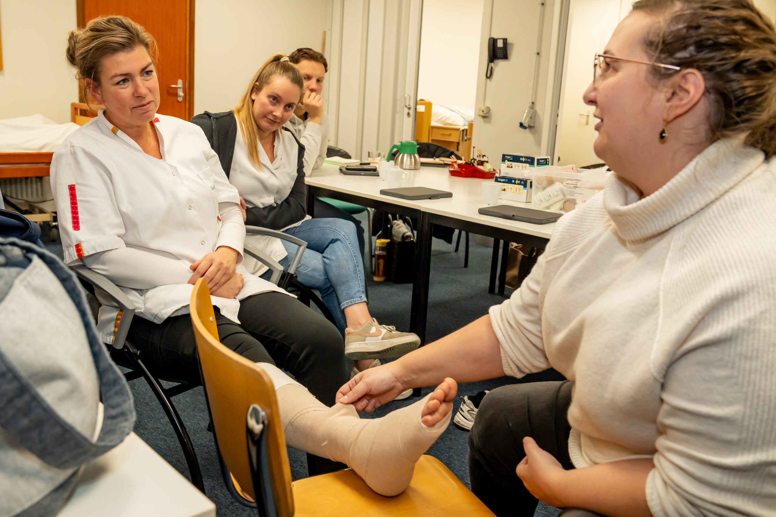 Zorgmedewerkers oefenen het zwachtelen van een voet tijdens een les in een praktijklokaal.