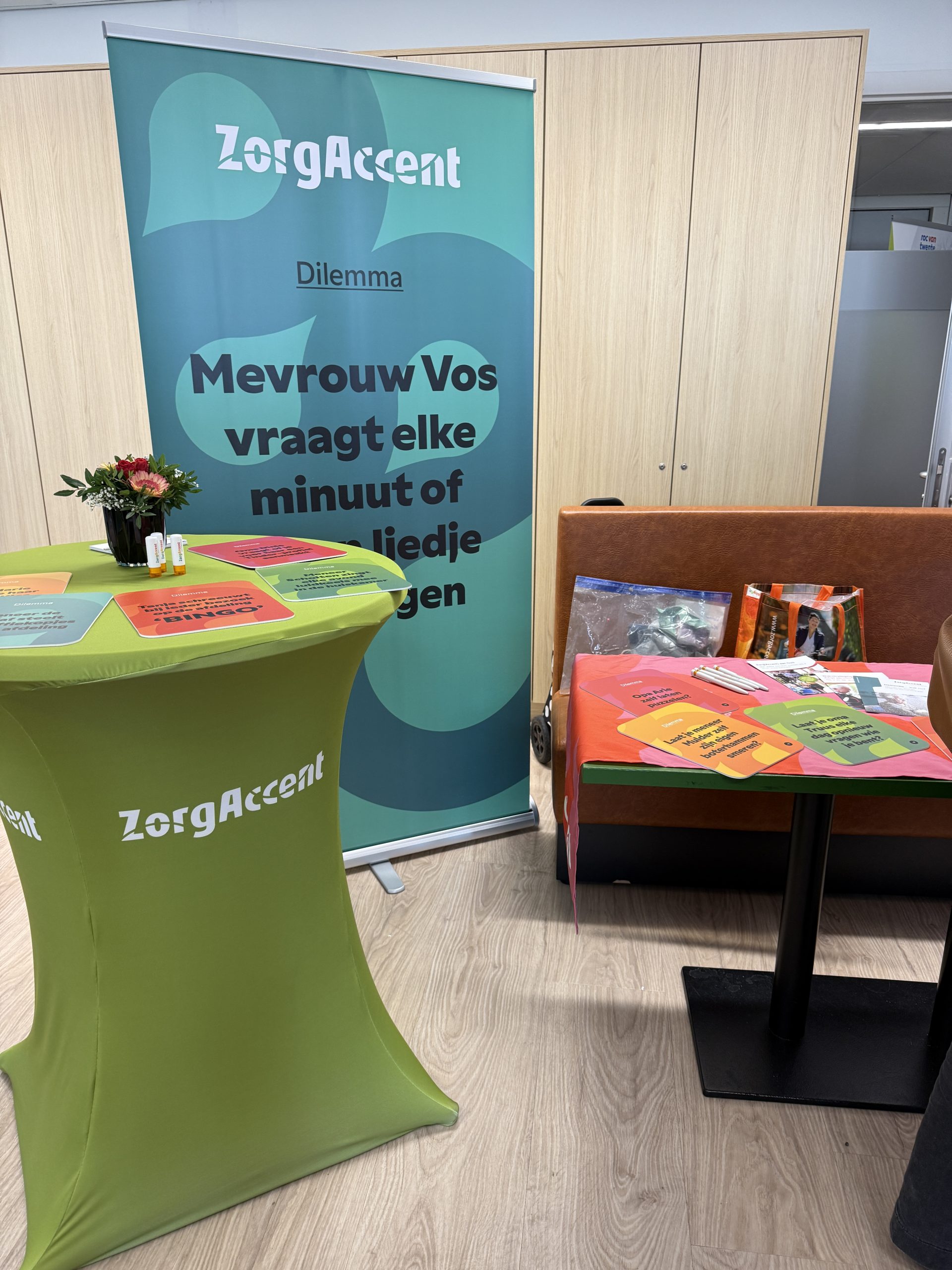 ZorgAccent-stand met groene statafel, banner met dilemma en kleurrijke kaartjes op tafel.